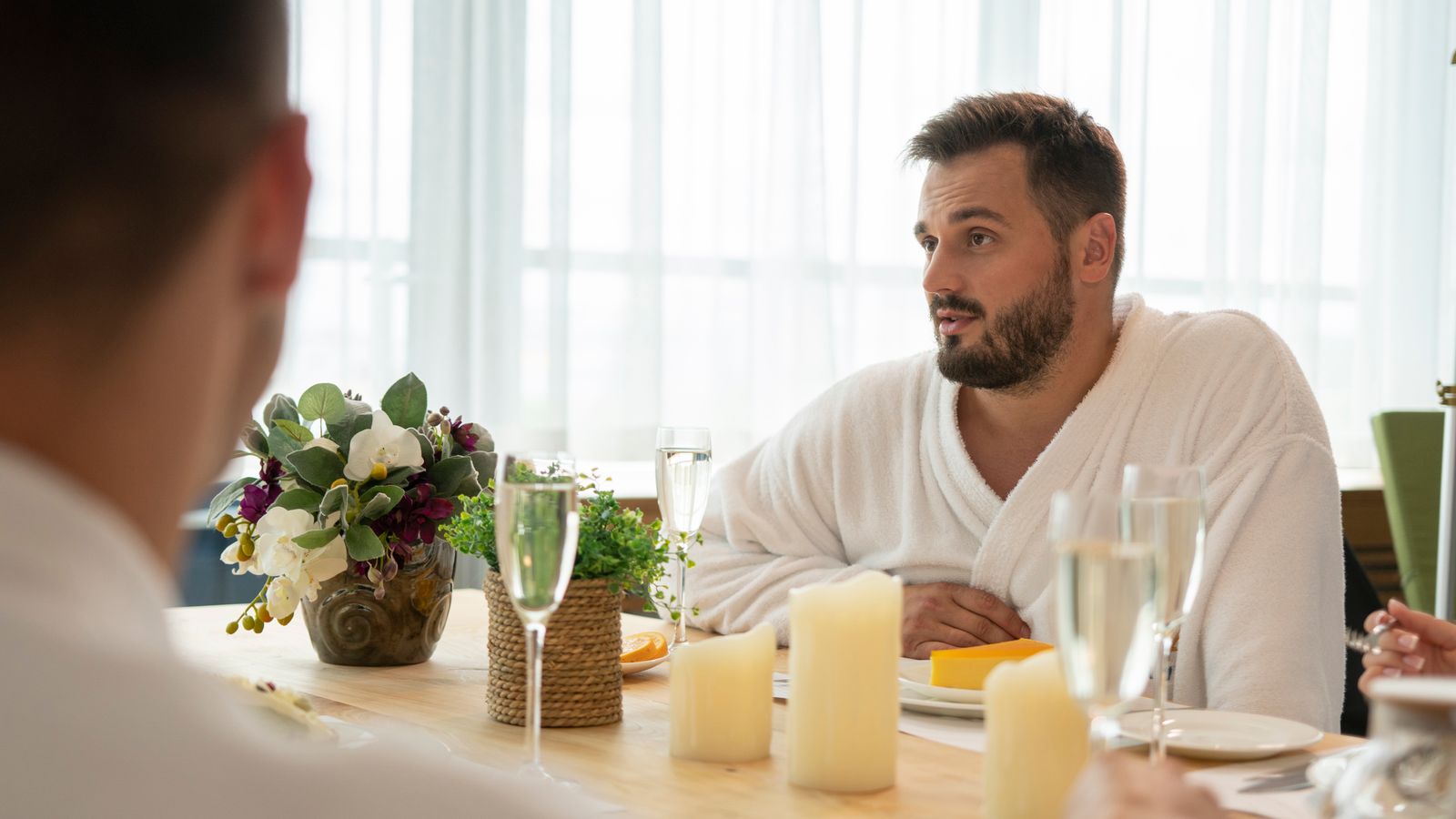 Two people talking over a relaxed breakfast table with flowers and candles